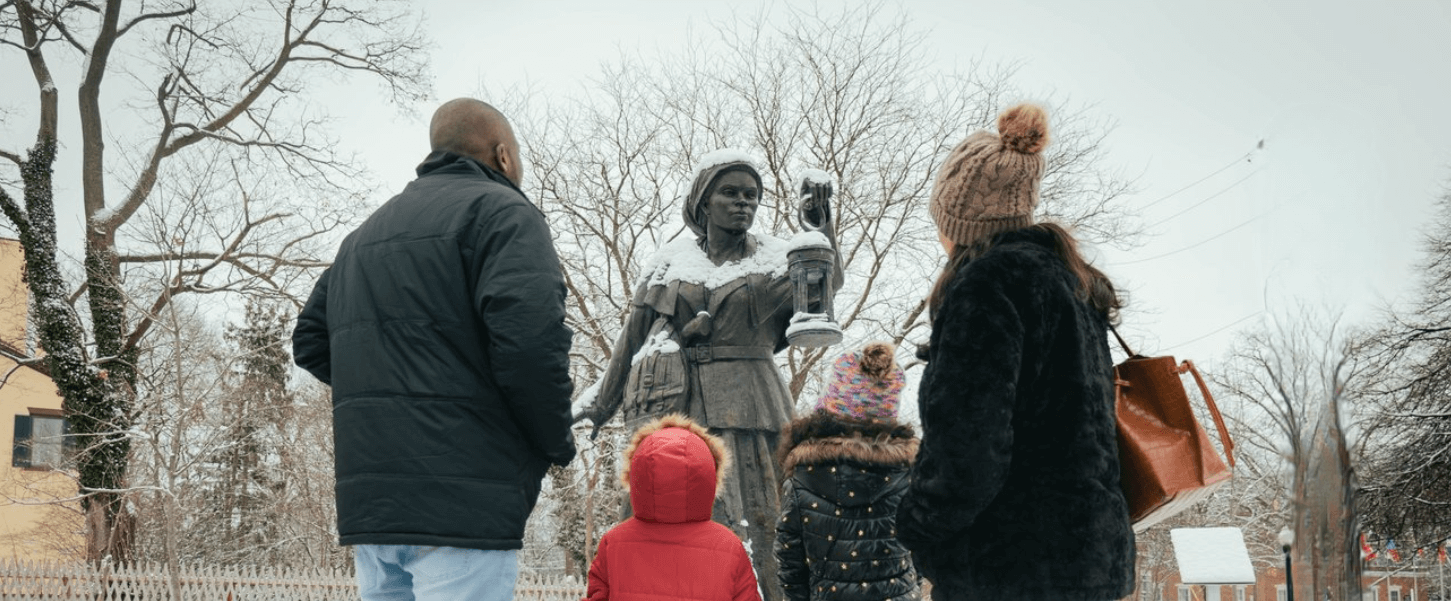 Family in standing in front of the Harriet Tubman Bronze Statue in the courtyard of the Equal Rights Heritage Center in the winter with snow in the ground